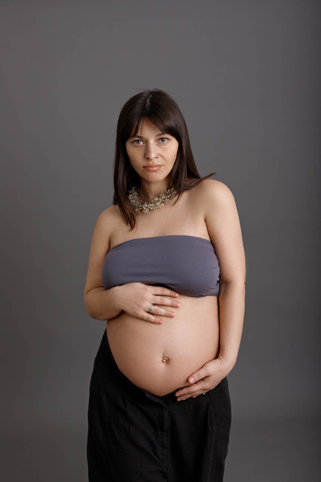 Pregnant woman cradling her bump on a grey backdrop — maternity session Tbilisi