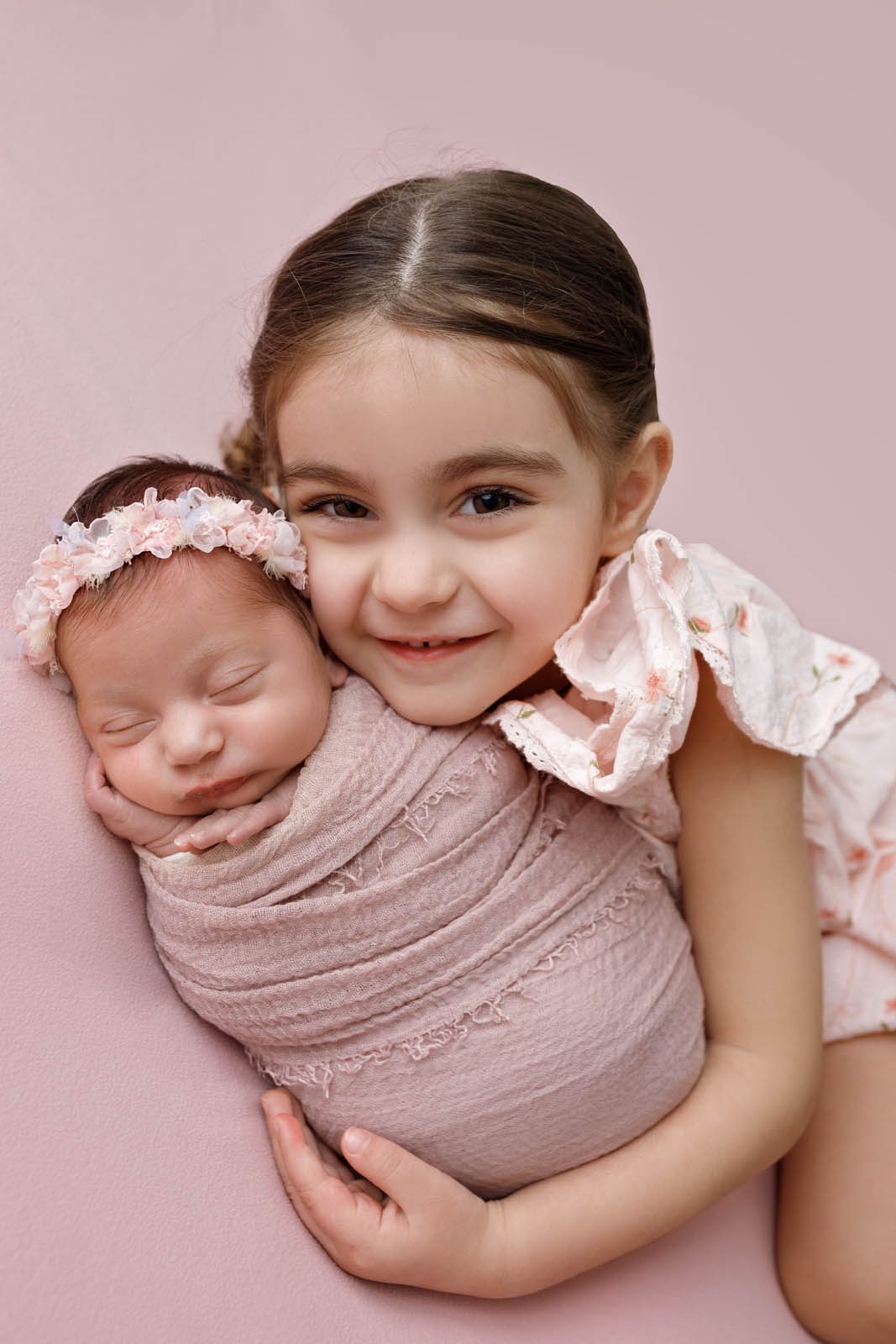 Young sister cuddling her newborn sibling on a soft pink backdrop — Tbilisi