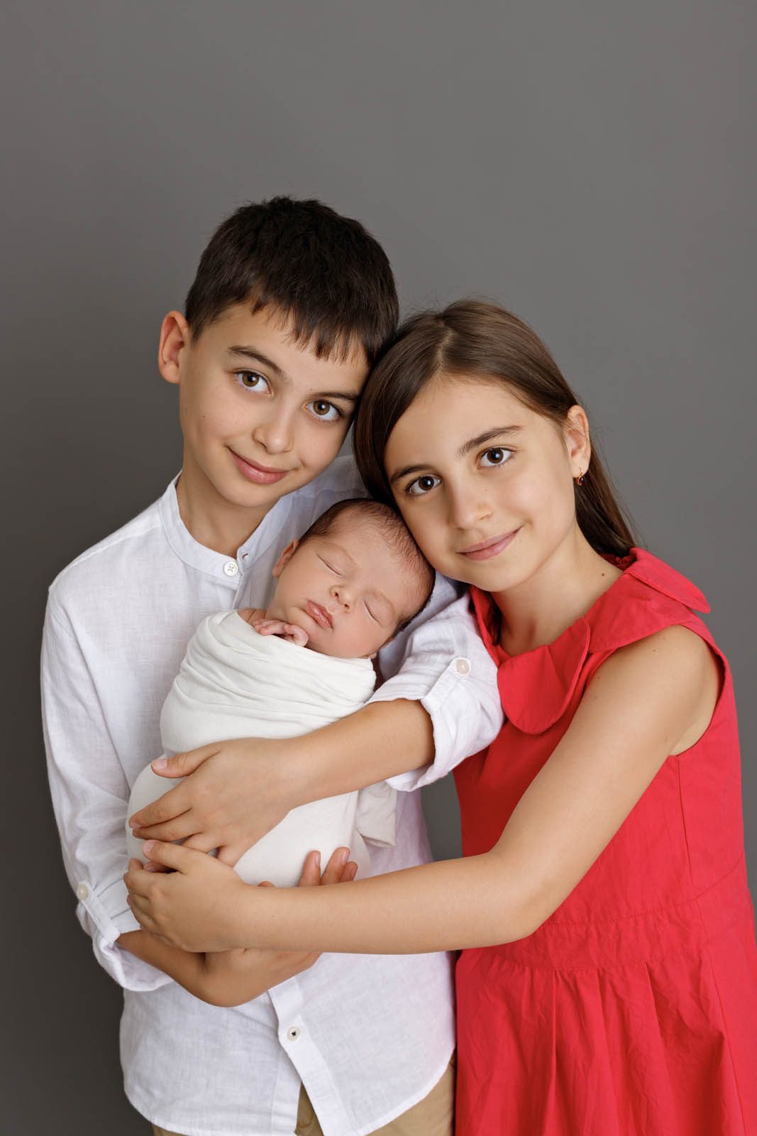 Brother and sister holding their newborn sibling — Tbilisi newborn studio