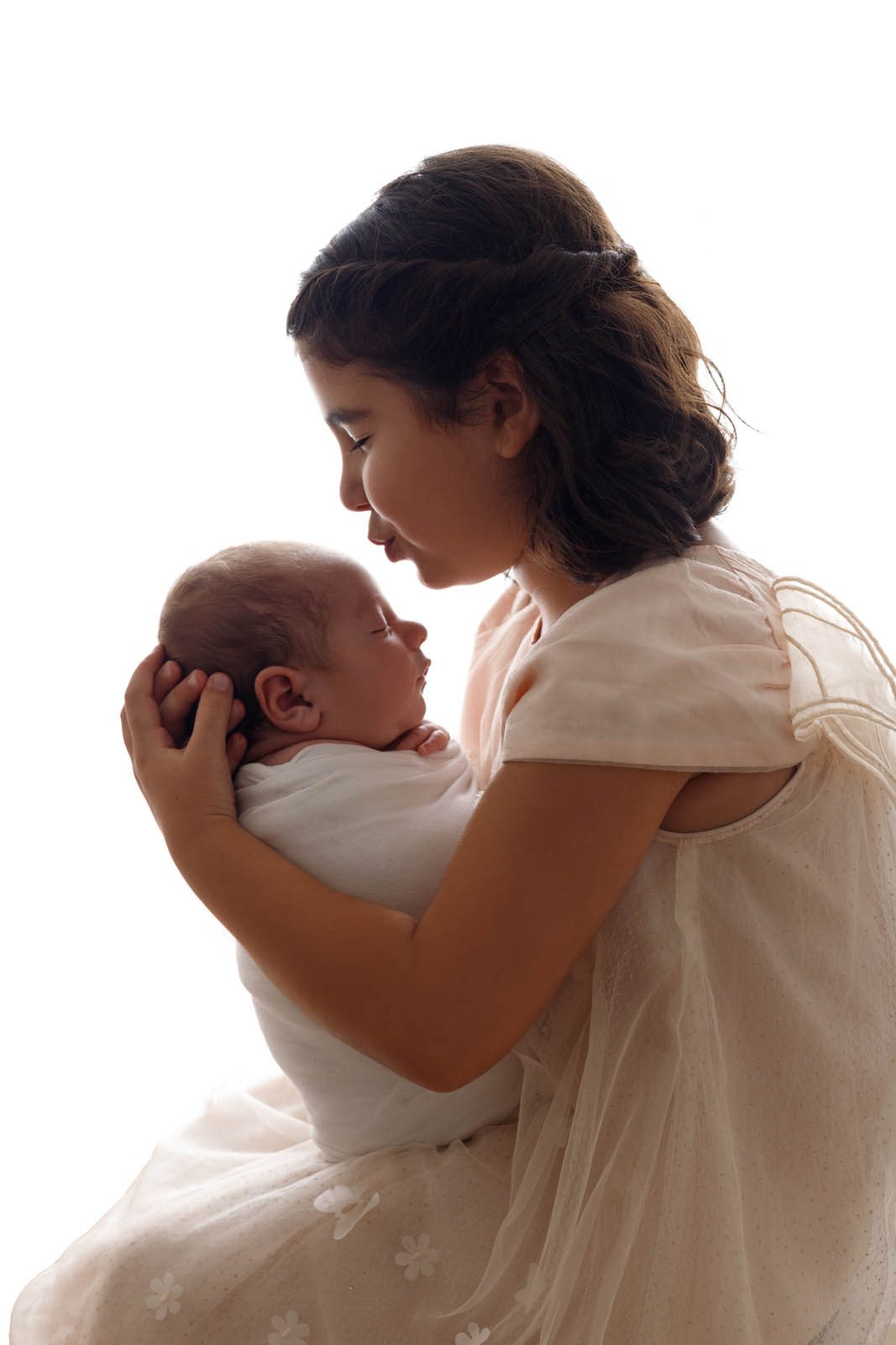 Older sister cradling her newborn sibling in soft light — Studio Muffin Tbilisi