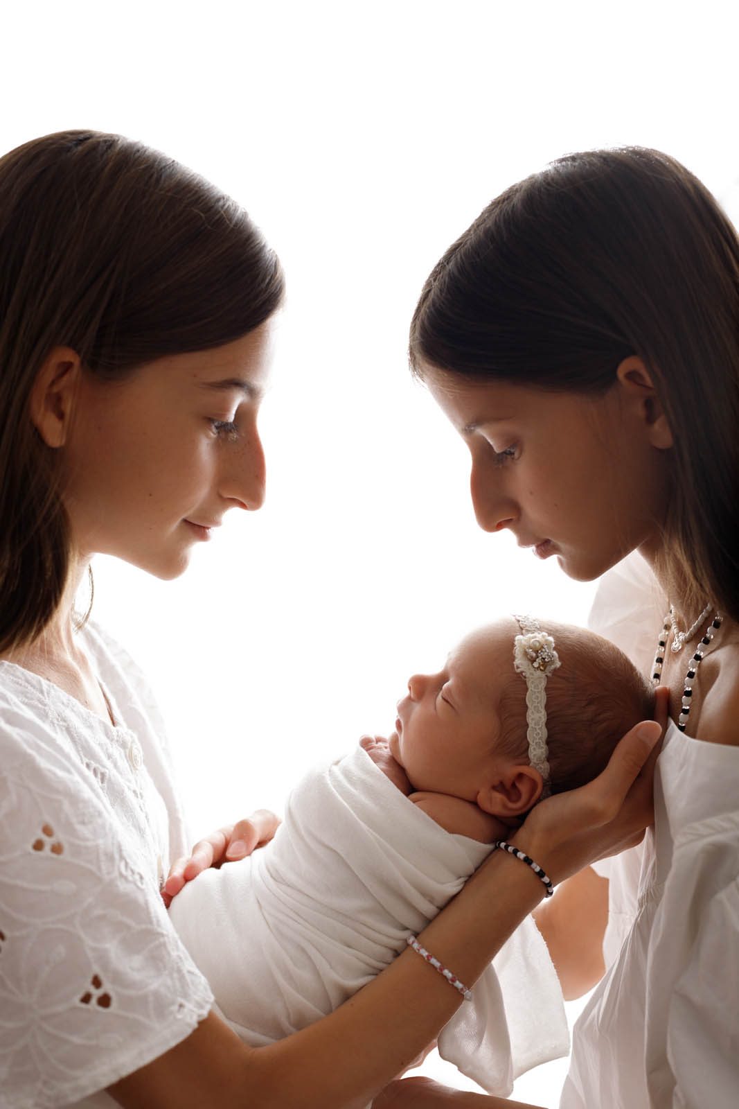 Two sisters gazing at their newborn sibling — Tbilisi newborn photography